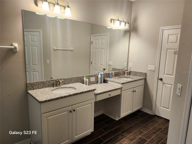 bathroom featuring wood finish floors, a sink, baseboards, and double vanity