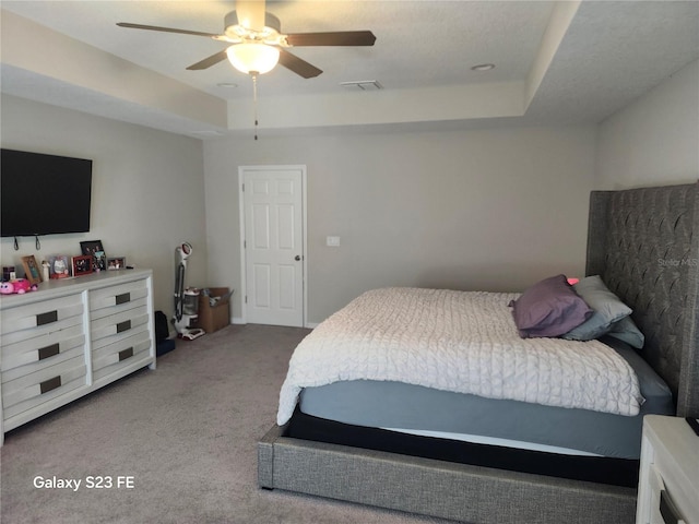 bedroom featuring carpet floors, a tray ceiling, visible vents, and a ceiling fan