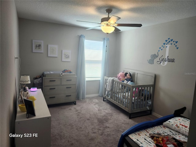 carpeted bedroom featuring a crib, baseboards, a ceiling fan, and a textured ceiling