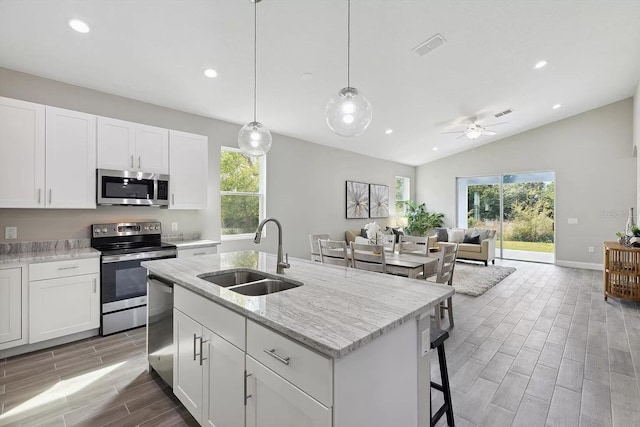 kitchen featuring stainless steel appliances, wood tiled floor, white cabinetry, a sink, and light stone countertops