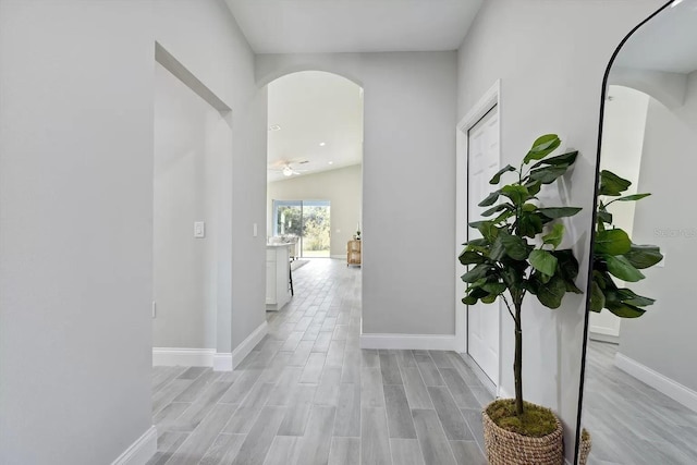 hallway featuring light wood-style flooring, arched walkways, and baseboards