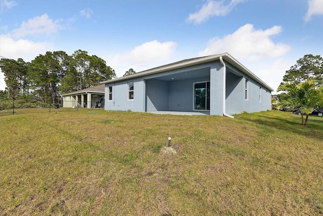 rear view of property featuring stucco siding, a lawn, and fence