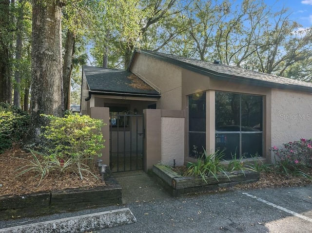 entrance to property with a shingled roof, a gate, and stucco siding