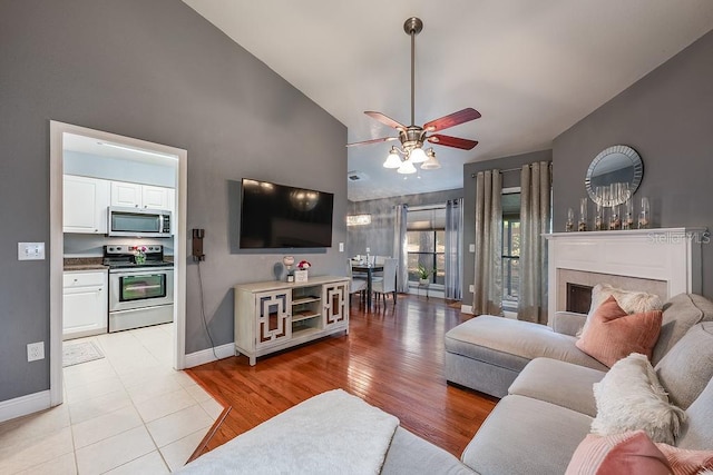 living room with a fireplace, ceiling fan, high vaulted ceiling, light wood-type flooring, and baseboards