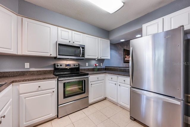 kitchen featuring light tile patterned floors, stainless steel appliances, dark countertops, white cabinets, and a textured ceiling