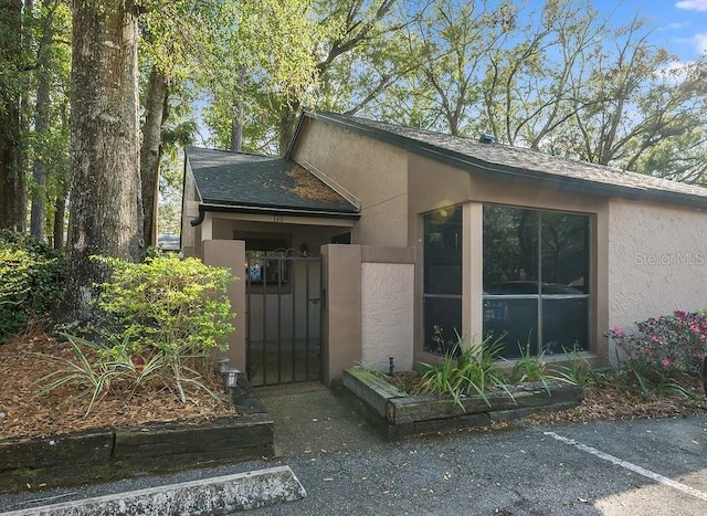 entrance to property featuring a gate, roof with shingles, and stucco siding