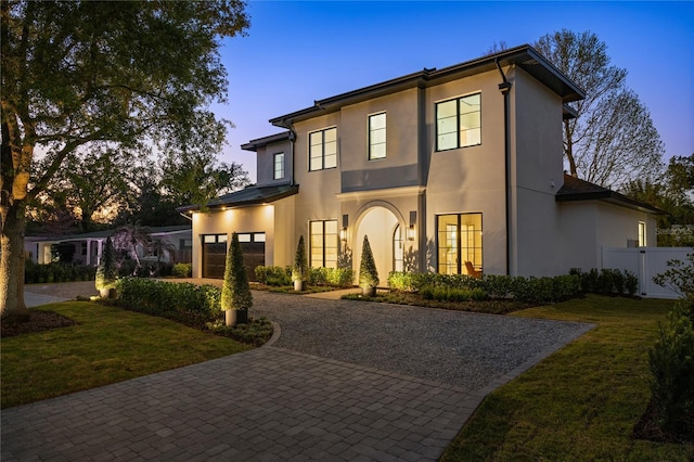 view of front of property with decorative driveway, fence, a yard, and stucco siding