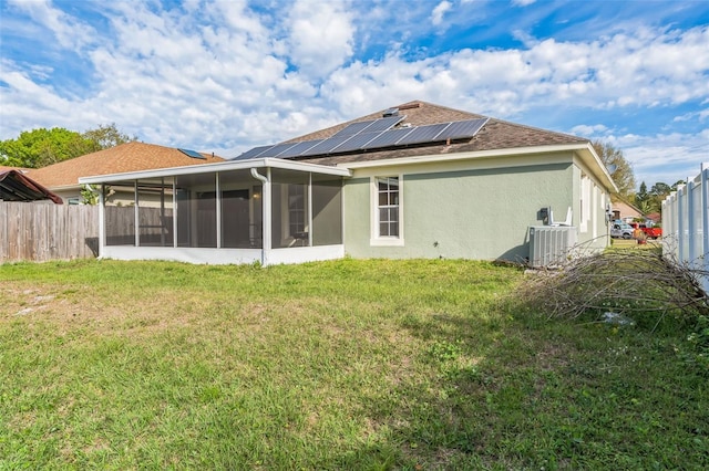 back of property with fence, central AC, a sunroom, a lawn, and roof mounted solar panels