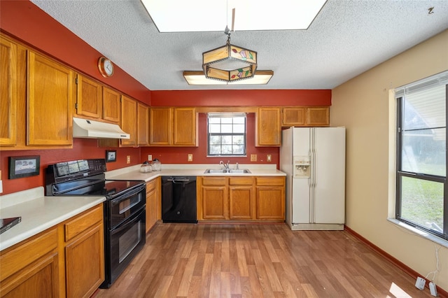 kitchen with under cabinet range hood, brown cabinets, black appliances, and a sink