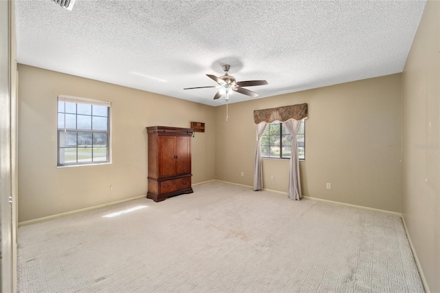 spare room featuring a textured ceiling, a ceiling fan, baseboards, and light carpet