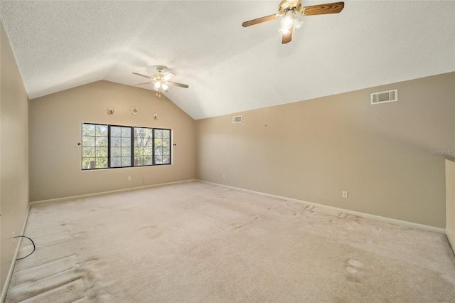 unfurnished room featuring visible vents, lofted ceiling, light colored carpet, and a textured ceiling