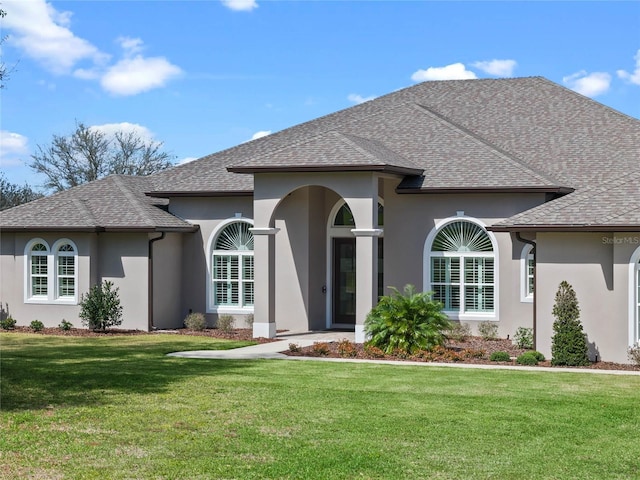 view of front of property with a shingled roof, a front yard, and stucco siding