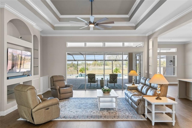 living area featuring crown molding, a tray ceiling, wood finished floors, and built in features