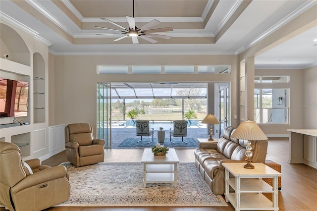 living area with a raised ceiling, wood finished floors, a sunroom, and built in features