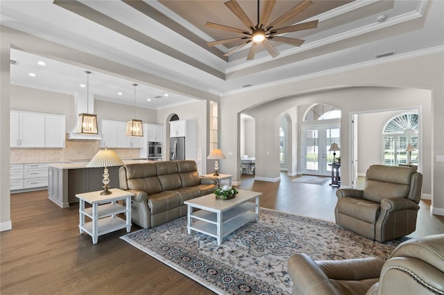 living area with ornamental molding, a tray ceiling, dark wood-style flooring, and arched walkways