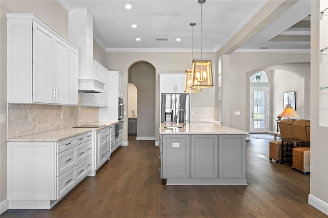 kitchen with arched walkways, a center island with sink, stainless steel refrigerator with ice dispenser, black electric stovetop, and a sink