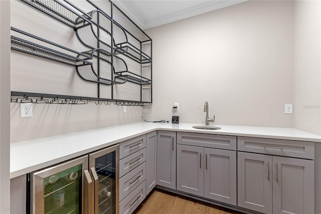 bar featuring crown molding, beverage cooler, a sink, and light wood-style flooring