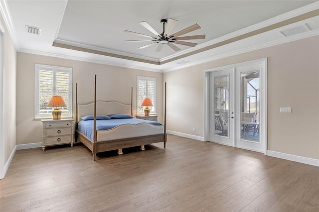 bedroom with access to outside, a tray ceiling, multiple windows, and light wood-style floors