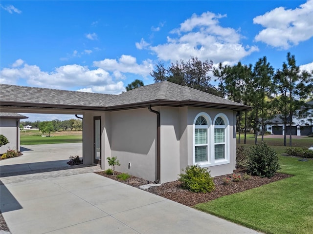 view of side of home with driveway, a yard, a shingled roof, and stucco siding