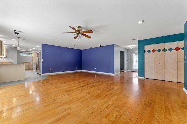 unfurnished living room with a ceiling fan, light wood-type flooring, a healthy amount of sunlight, and baseboards