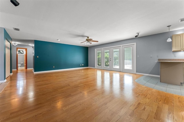 unfurnished living room featuring light wood-style flooring, visible vents, a ceiling fan, baseboards, and french doors