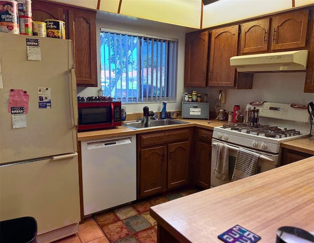 kitchen featuring white appliances, under cabinet range hood, light countertops, and a sink