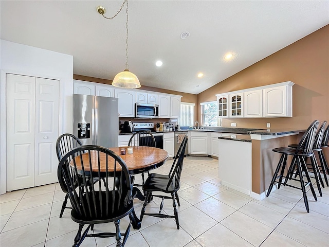 kitchen featuring dark countertops, stainless steel appliances, a peninsula, light tile patterned floors, and glass insert cabinets