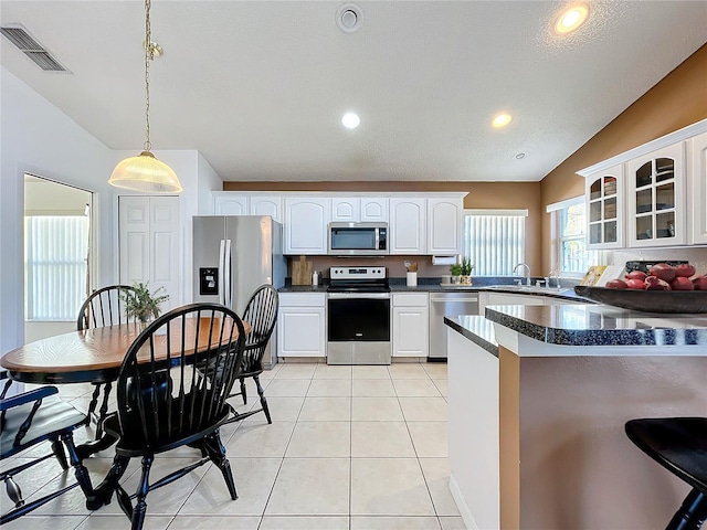 kitchen with dark countertops, visible vents, glass insert cabinets, light tile patterned flooring, and stainless steel appliances