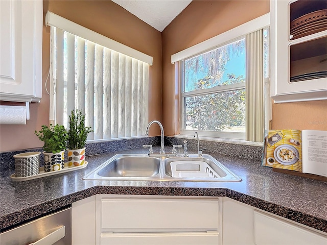 kitchen with dishwasher, dark countertops, white cabinetry, and a sink