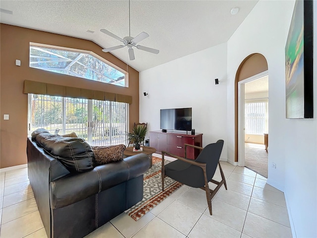 living area with high vaulted ceiling, a ceiling fan, a textured ceiling, light tile patterned flooring, and baseboards