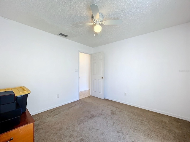 carpeted empty room with baseboards, a ceiling fan, visible vents, and a textured ceiling