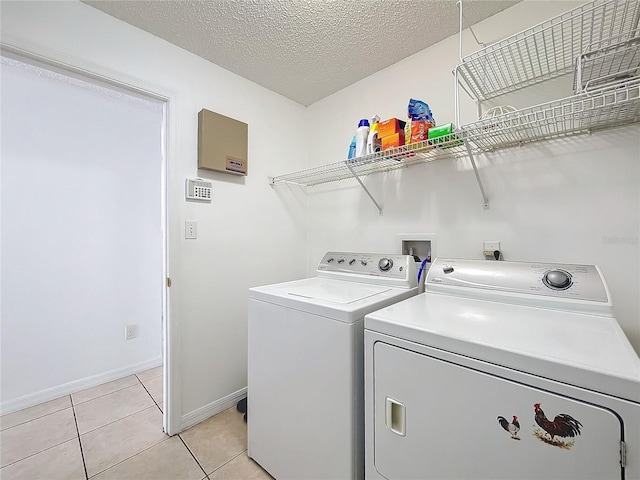 clothes washing area featuring a textured ceiling, separate washer and dryer, light tile patterned floors, baseboards, and laundry area