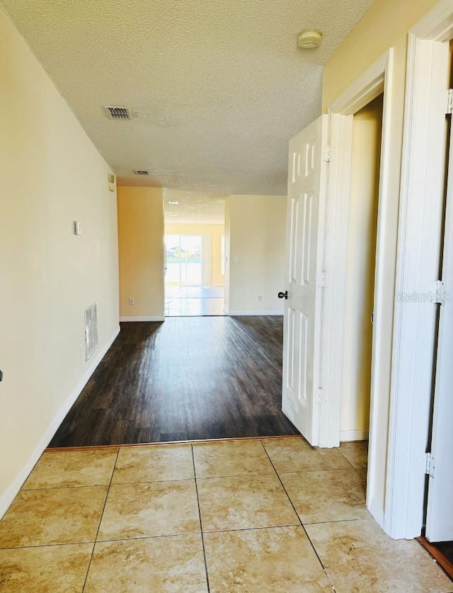 hallway with tile patterned flooring, visible vents, a textured ceiling, and baseboards