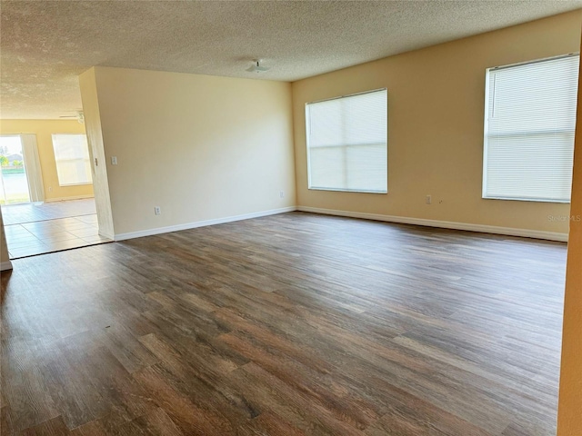 empty room featuring dark wood-type flooring, a textured ceiling, and baseboards