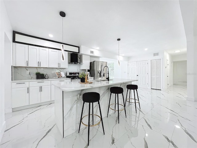 kitchen with stainless steel appliances, a sink, marble finish floor, wall chimney range hood, and decorative backsplash