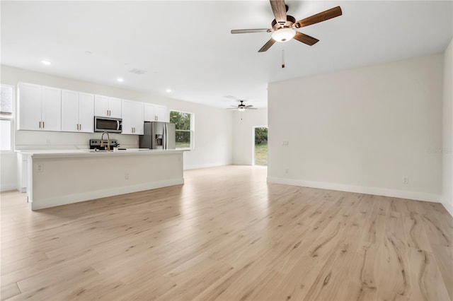 kitchen with open floor plan, appliances with stainless steel finishes, an island with sink, and light wood finished floors