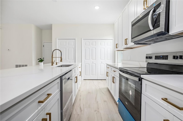 kitchen with visible vents, stainless steel appliances, light countertops, light wood-type flooring, and a sink