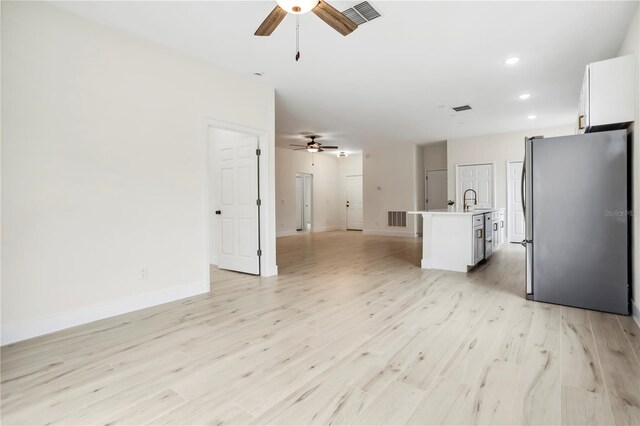 kitchen featuring a kitchen island with sink, visible vents, white cabinetry, open floor plan, and freestanding refrigerator