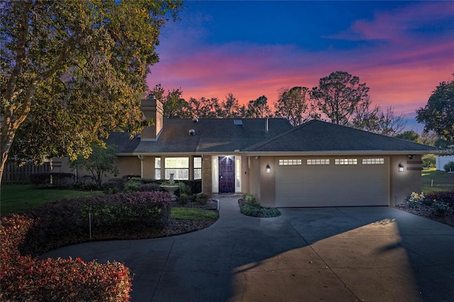 ranch-style home featuring a garage, a shingled roof, concrete driveway, stucco siding, and a chimney