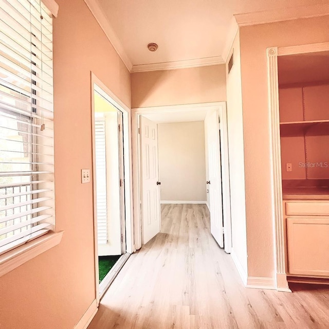 corridor featuring light wood finished floors, visible vents, baseboards, and crown molding