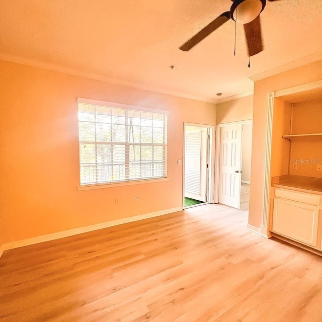 spare room featuring ornamental molding, light wood-type flooring, ceiling fan, and baseboards