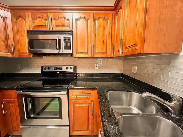 kitchen featuring brown cabinets, stainless steel appliances, decorative backsplash, a sink, and dark stone countertops