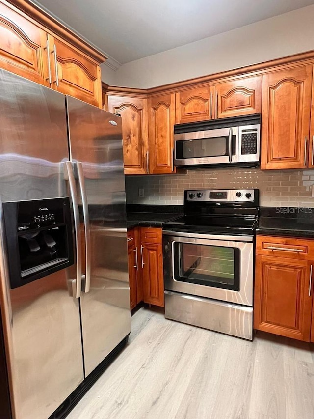 kitchen featuring stainless steel appliances, dark countertops, brown cabinets, and light wood finished floors