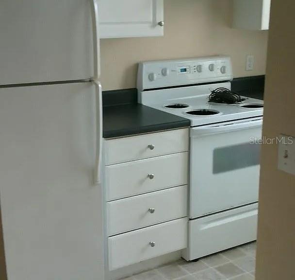 kitchen with dark countertops, white appliances, and white cabinets