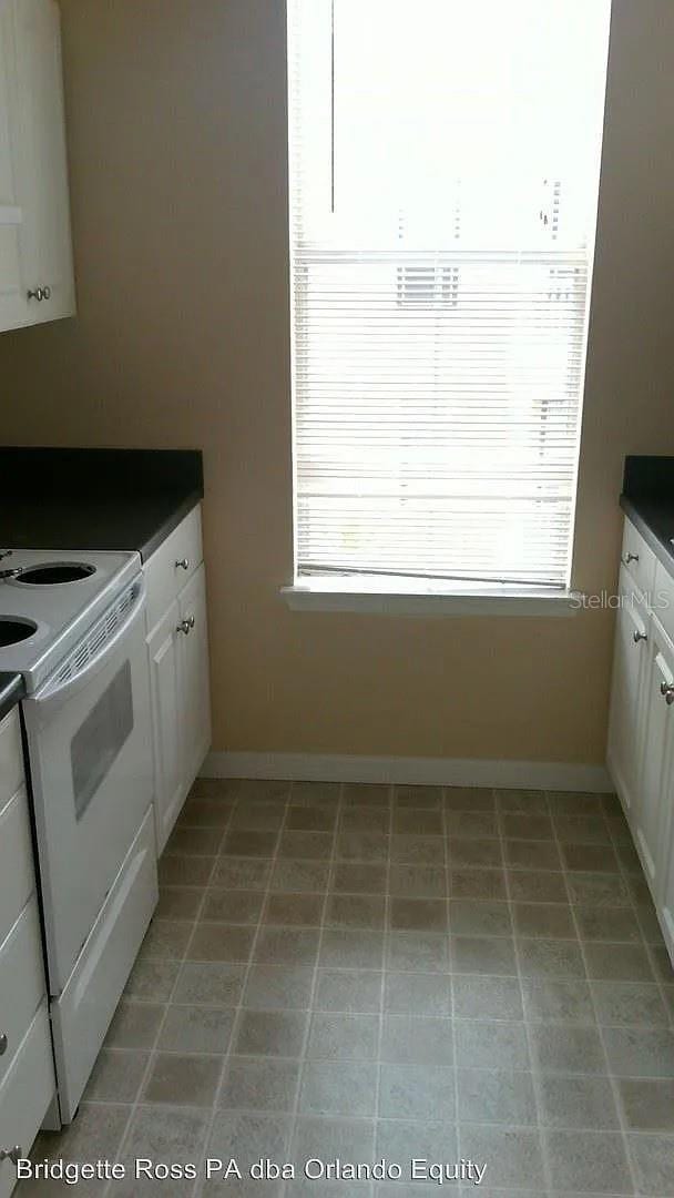 kitchen featuring dark countertops, baseboards, white cabinets, and white electric range