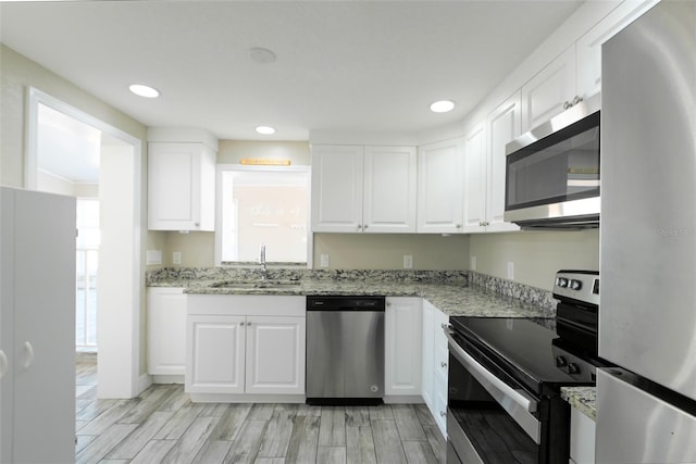 kitchen with light stone counters, wood tiled floor, stainless steel appliances, white cabinetry, and a sink