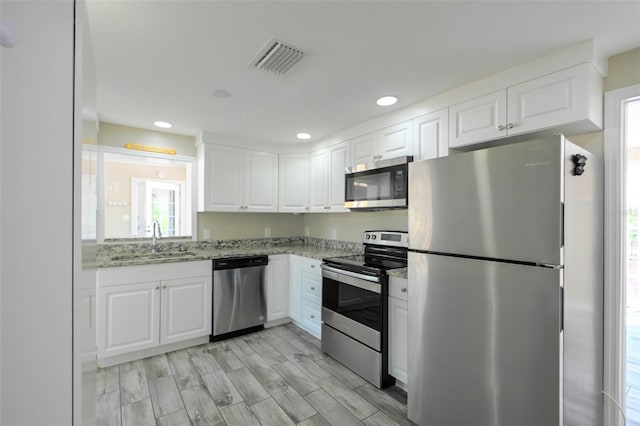 kitchen featuring light stone counters, stainless steel appliances, a sink, visible vents, and white cabinets