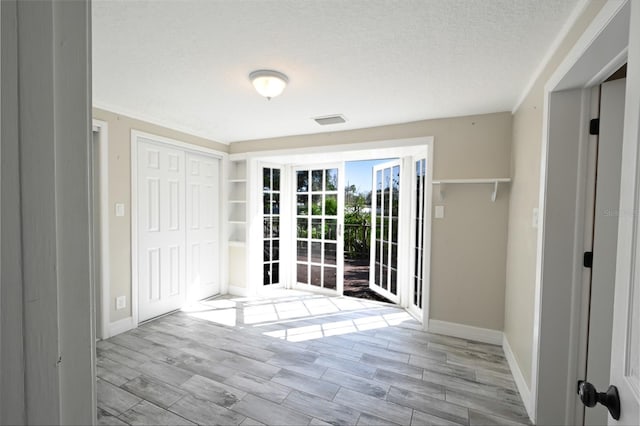 interior space with wood tiled floor, visible vents, a textured ceiling, and baseboards