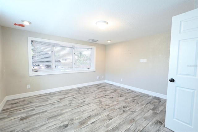 spare room featuring light wood-style flooring, visible vents, and baseboards