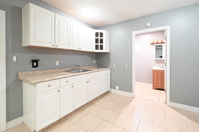 kitchen featuring white cabinets, baseboards, light countertops, and a sink